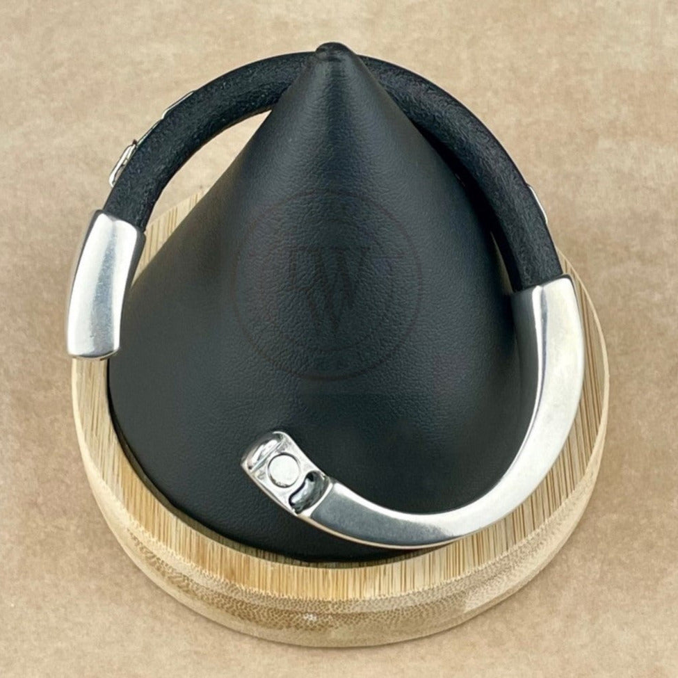 This unisex bracelet features a sleek black leather band adorned with a delicate rhodium chain for a refined yet edgy look. The bracelet is secured with a long, arcing, antique silver magnetic clasp, ensuring easy wear and a seamless fit. The combination of textures—smooth leather, polished metal, and subtle chain detailing—creates a versatile piece that balances rugged charm with modern sophistication.