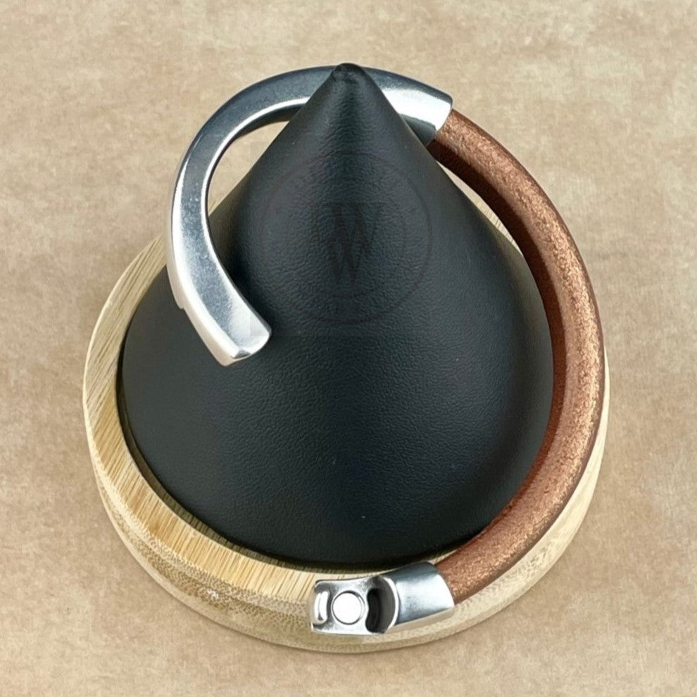 The bracelet features a matte metallic copper leather band, elegantly curved with a long, arcing, antique silver magnetic clasp. Displayed on a black conical stand with a natural wood base, it blends warm tones with sleek silver. The ergonomic clasp ensures a secure and comfortable fit, while the rich leather texture contrasts beautifully with the smooth silver for a bold yet timeless look.
