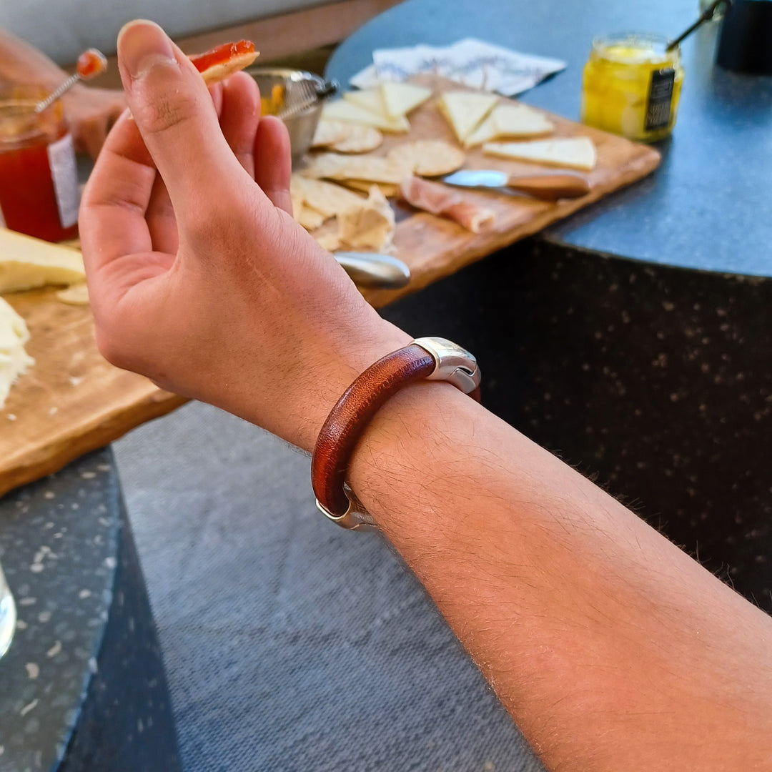 A man wearing a leather bracelet with a blurred background of food items on a table. Cobo bracelet lifestyle photo.