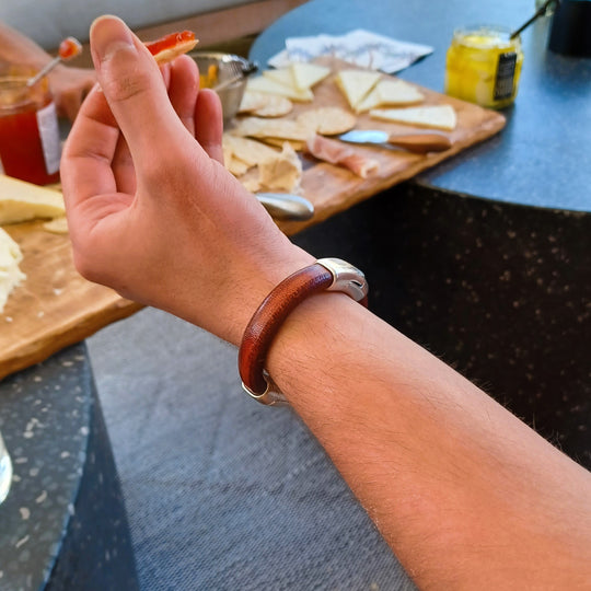 A man wearing a leather bracelet with a blurred background of food items on a table. Cobo bracelet lifestyle photo.