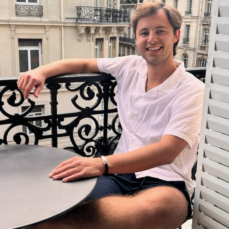 Man sitting at a table on a balcony with a cityscape background. Cobo bracelet lifestyle photo