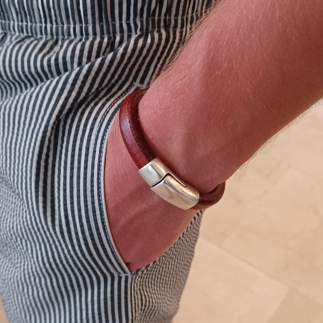Brown leather bracelet with silver clasp on a person's wrist, wearing  striped shorts. Cobo bracelet lifestyle photo.
