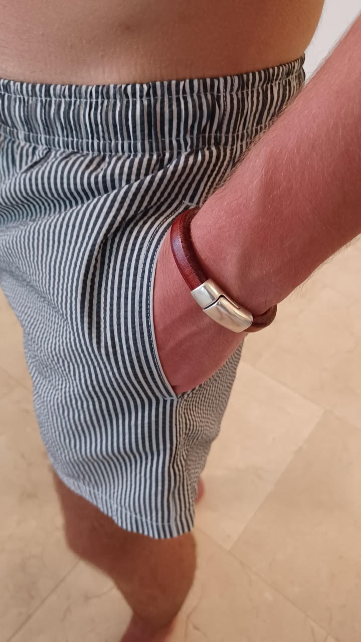 Brown leather bracelet with silver clasp on a person's wrist, wearing  striped shorts. Cobo bracelet lifestyle photo.