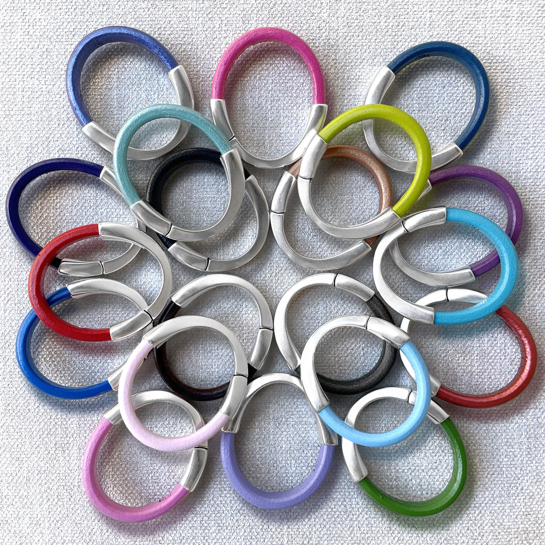 A multi-colored kaleidoscope of Arena leather bracelets displayed like a flower head on light gray fabric.