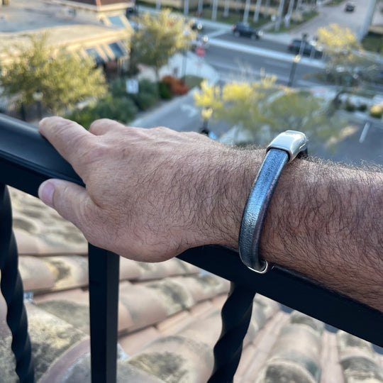 A wrist wearing a metallic silver-black leather bracelet on a balcony railing overlooking a street. Cobo bracelet lifestyle photo