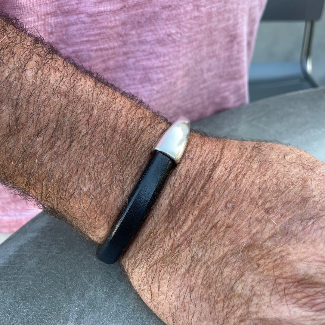 Black leather Arena bracelet with a silver clasp on a wrist with a blurred background. Arena bracelet lifestyle photo.