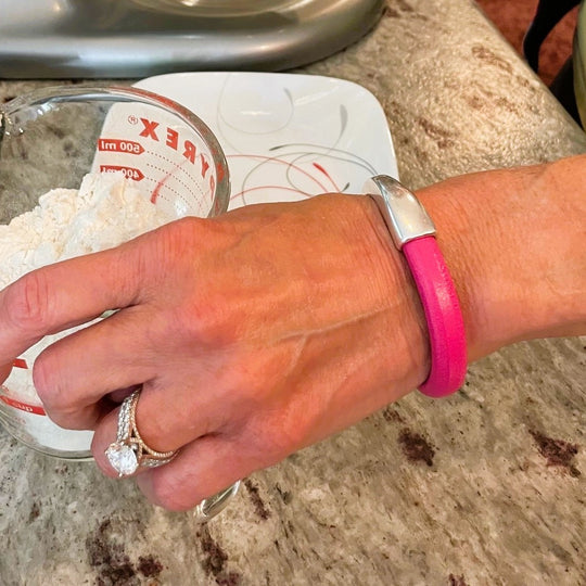 A hand holding a measuring cup with flour on a kitchen counter, and wearing a pink leather Arena bracelet with a silver clasp. Arena bracelet lifestyle photo.