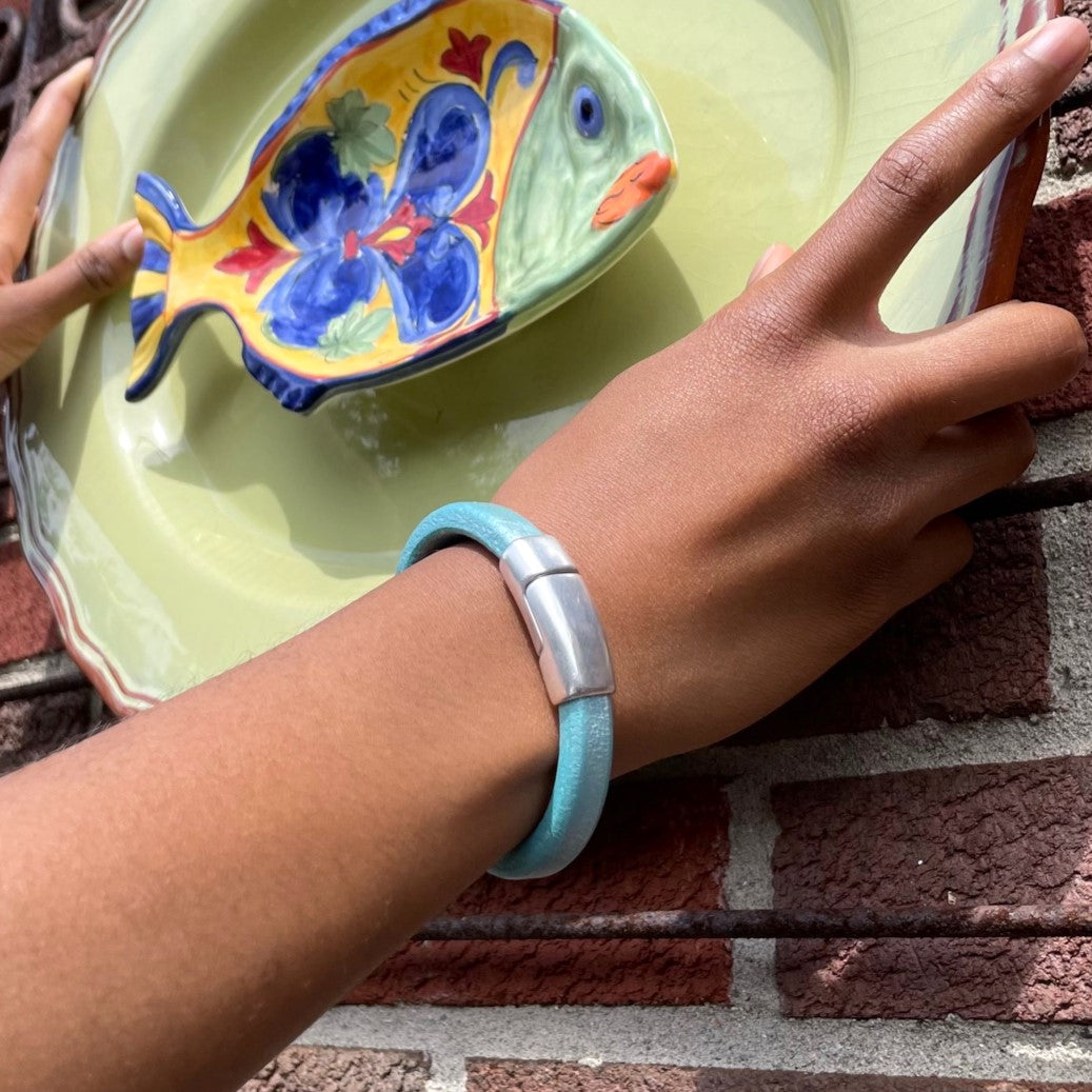 A close-up of a person wearing a blue leather Cobo bracelet while hanging a colorful ceramic fish on a green plate on a brick wall. Cobo bracelet lifestyle photo.