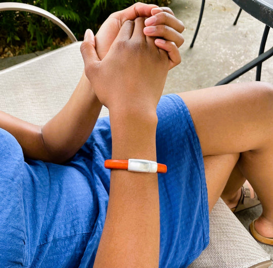A person wearing a blue dress with an orange leather Cobo bracelet, sitting on a chair. Cobo bracelet lifestyle photo.