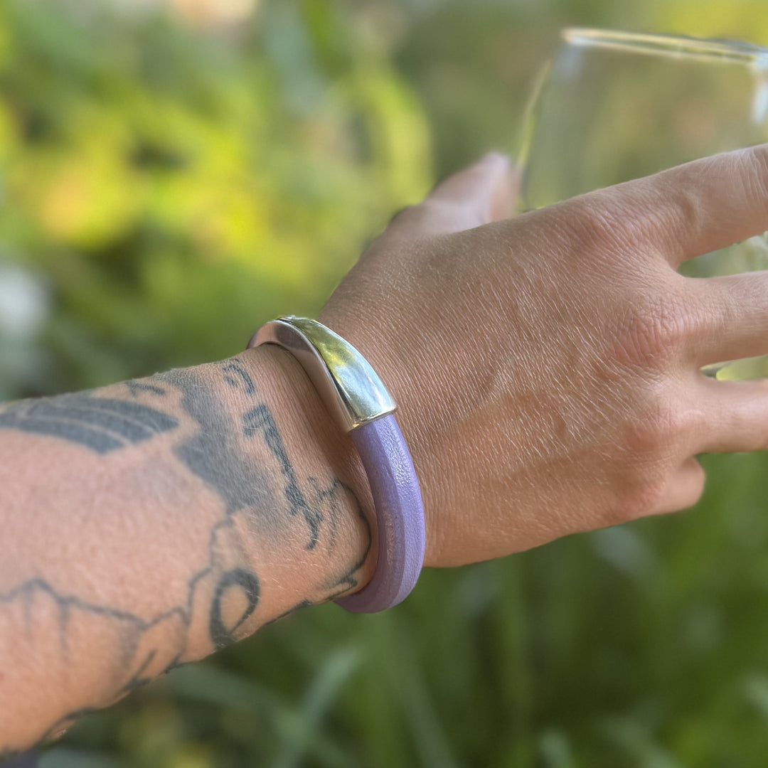 Hand wearing a purple bracelet with a silver clasp against a blurred green background