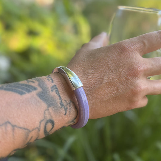 Hand wearing a purple bracelet with a silver clasp against a blurred green background