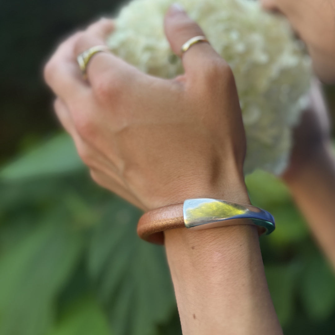 Hand wearing a bracelet with a blurred background of greenery