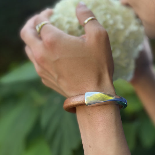 Hand wearing a bracelet with a blurred background of greenery