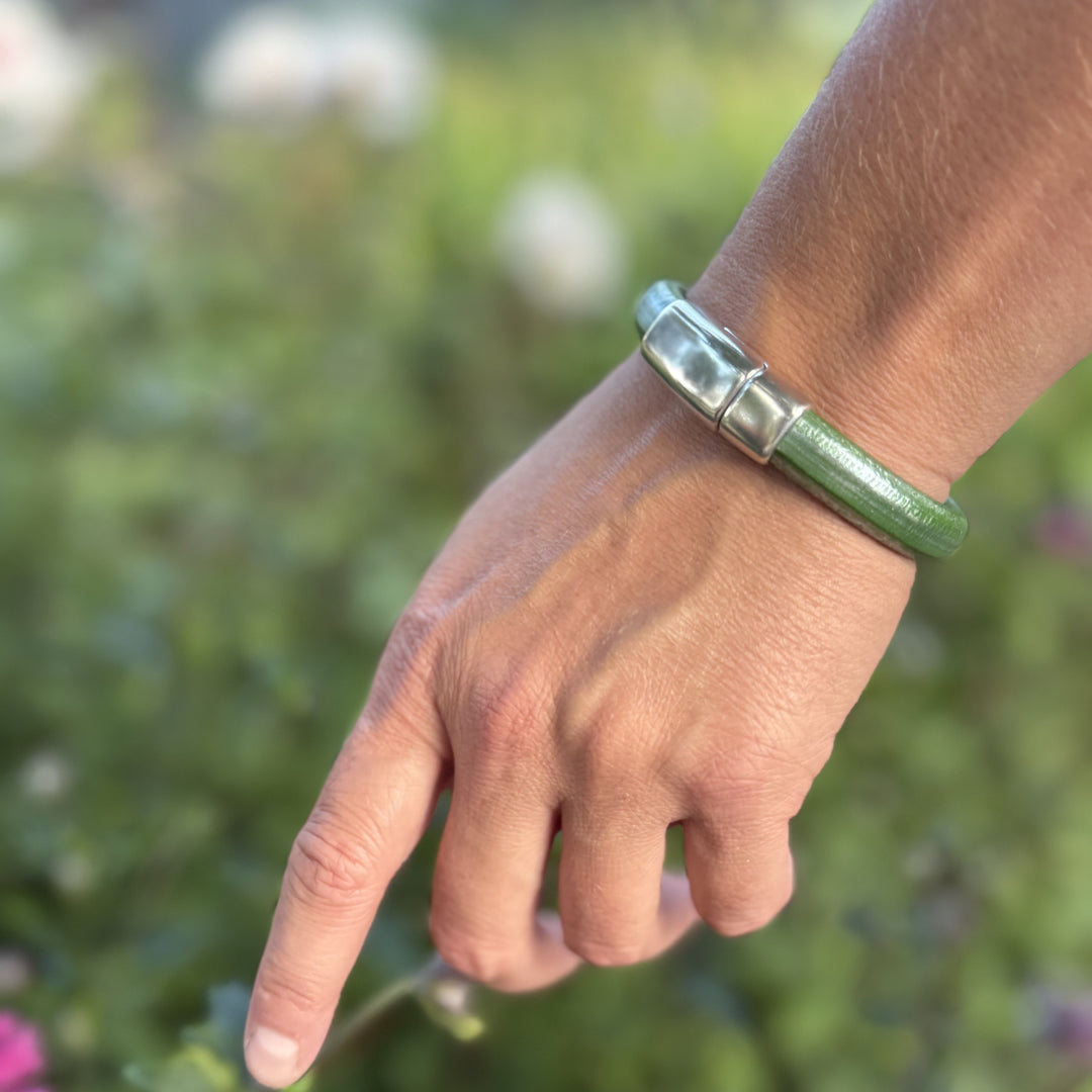Hand wearing a green bracelet with a blurred natural background