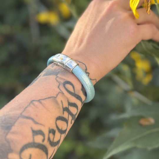 Person's arm with tattoos wearing a light blue bracelet against a blurred natural background