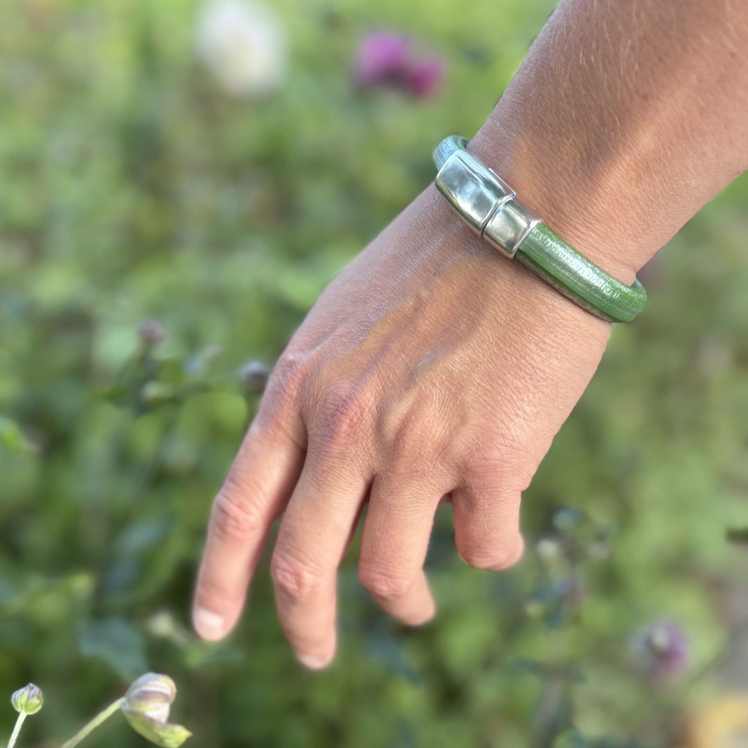 Hand wearing a green bracelet with a blurred natural background