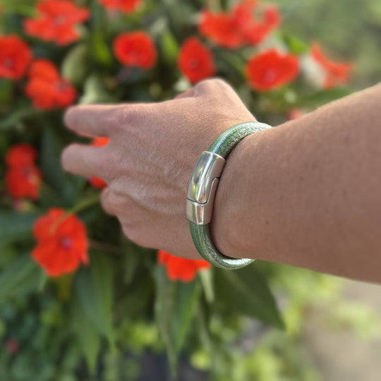 Hand wearing a green bracelet with red flowers in the background