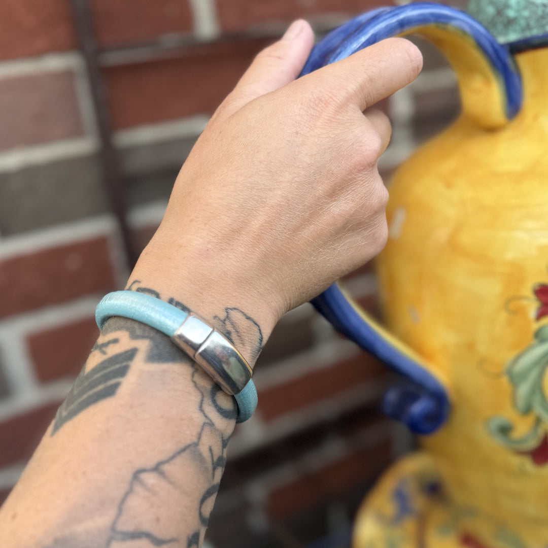 Hand holding a blue handle with a tattooed arm, wearing a blue bracelet, against a brick wall.