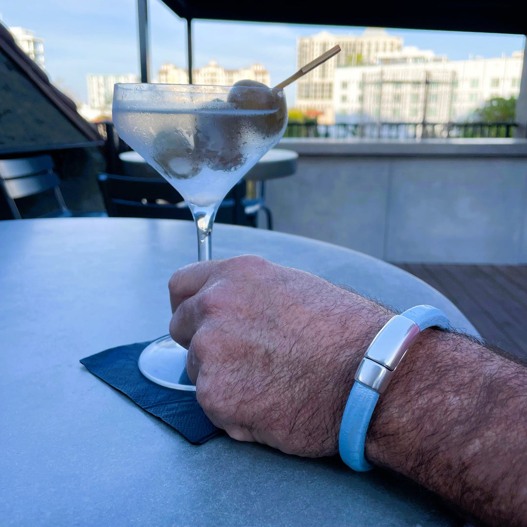 Light blue bracelet worn on a man holding a martini in a rooftop bar overlooking the city.
