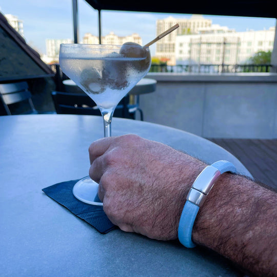 Light blue bracelet worn on a man holding a martini in a rooftop bar overlooking the city.